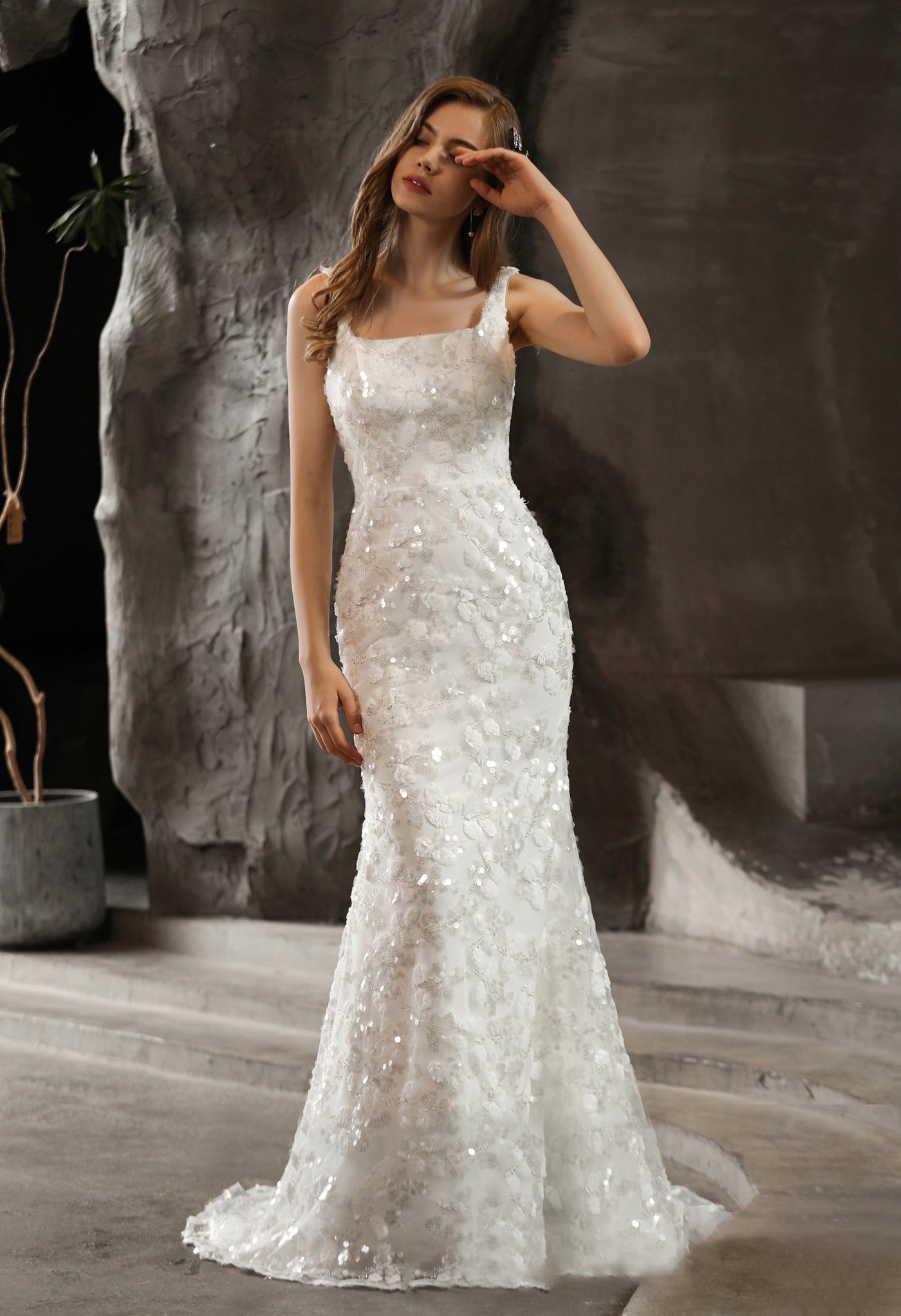 A woman posing in an elegant white Sequined Lace Square Neckline Sheath Wedding Dress by Bergamot Bridal.
