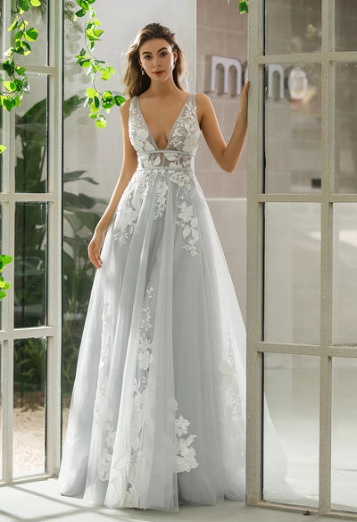 A woman in a grey Plunging V-Neck A-Line Ball Gown Bridal Gown from Bergamot Bridal, posing in front of a window.