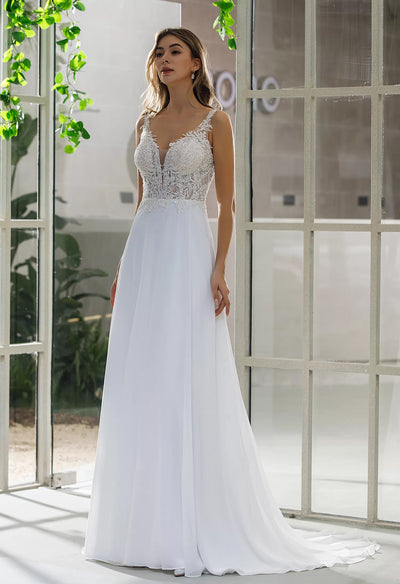 A bride in an Illusion Bodice Chiffon Skirt A-Line Bridal Gown from Bergamot Bridal standing in front of a window.