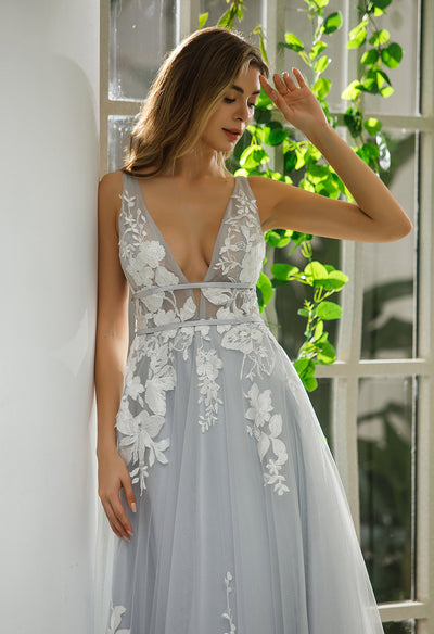A woman in a grey wedding dress leaning against a window at Bergamot Bridal, wearing the Plunging V-Neck A-Line Ball Gown Bridal Gown.
