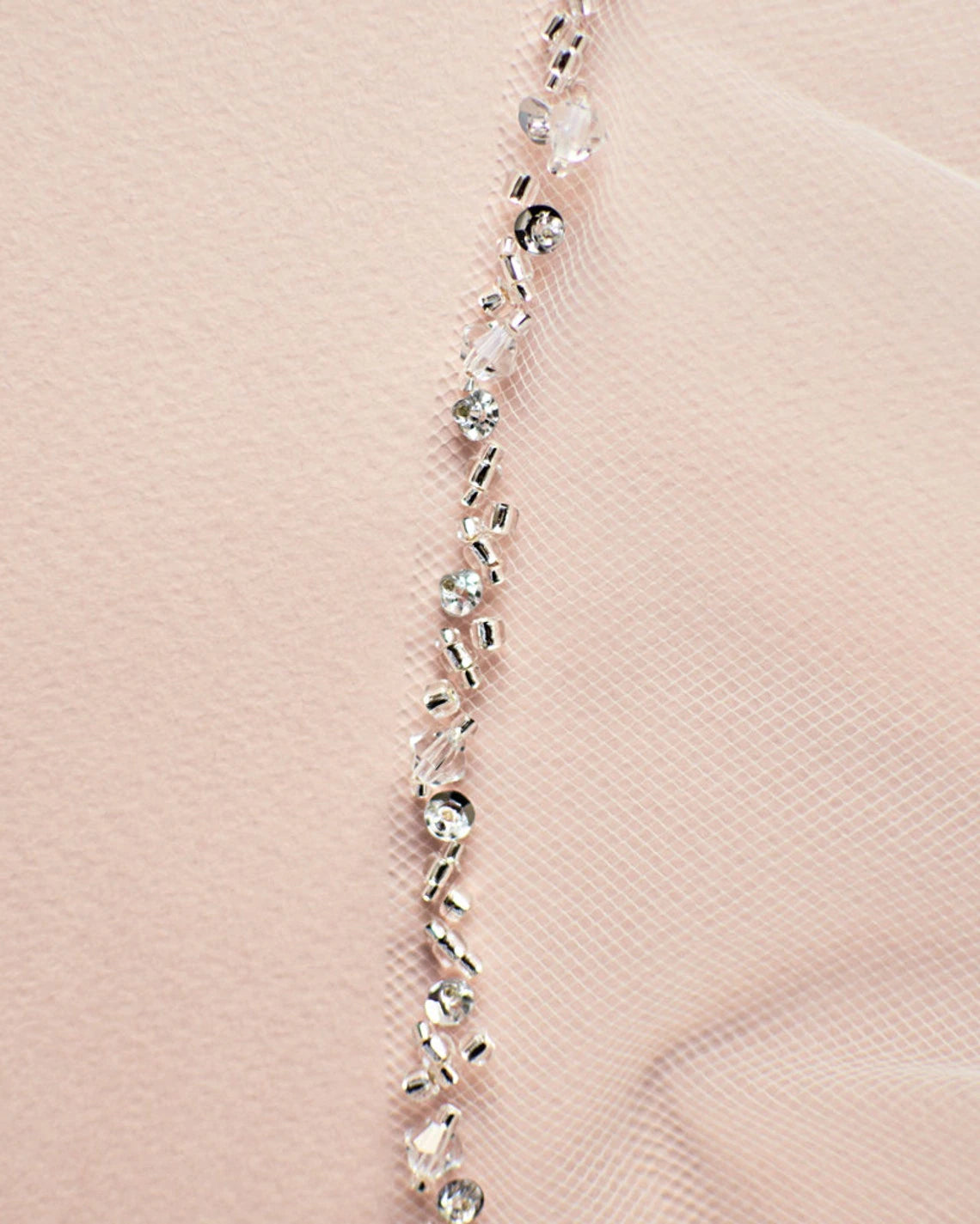 Close-up of a delicate pink wedding dress fabric with a zigzagging line of Bergamot Bridal's Fingertip Length Crystal Beaded Veil adding sparkle and decoration.
